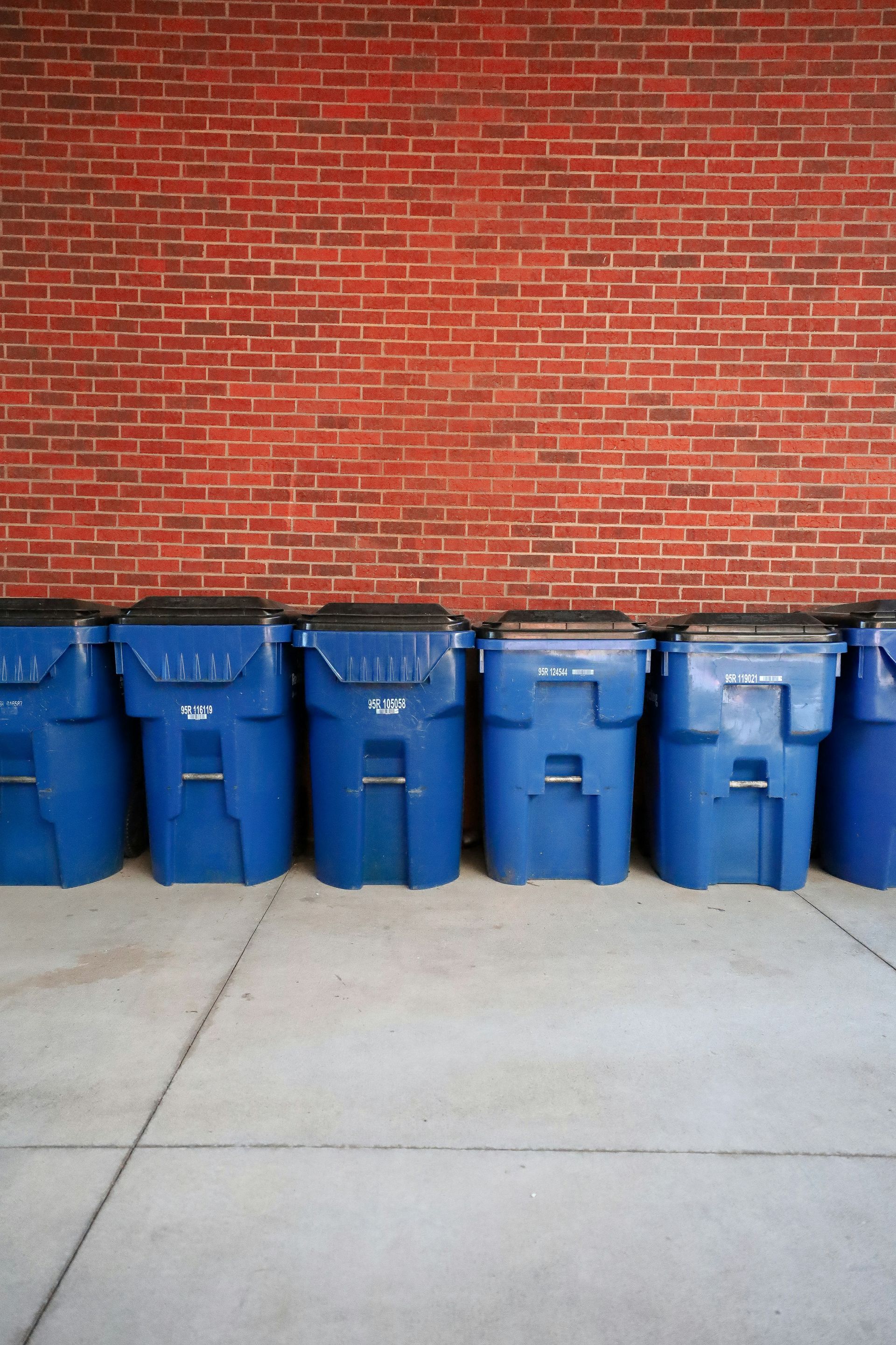 A row of blue trash cans sitting in front of a brick wall